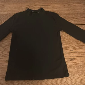 Svart ribbad tröja - Säljer en stilren svart ribbad tröja i storlek 160. Perfekt för både vardag och festliga tillfällen. Tröjan har långa ärmar och en hög krage som ger en elegant touch. Passar bra till jeans eller kjol för en snygg look. Hör av dig vid intresse!