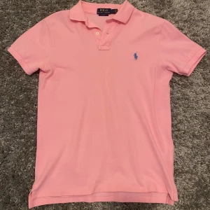 Rosa pikétröja från Ralph Lauren - Säljer en snygg rosa pikétröja från Ralph Lauren i slim fit. Den har en klassisk krage med två knappar och det ikoniska blå logotypbroderiet på bröstet. Nypris: 1299, mitt pris: 499. Storlek: S. Bra skick, 9/10 använd ett fåtal gånger. Köpare står för frakten📦