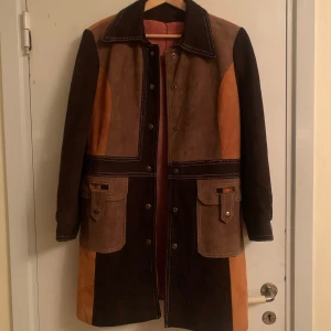 Retro kappa - Äkta retro mockakappa i brunt, beiget och oranget. Den har knappar framtill och stora fickor. Jättebra skick. Perfekt vintage- och höstälskare! Skriv privat för fler bilder och frågor! Säljs pga för liten i ärmen🍁