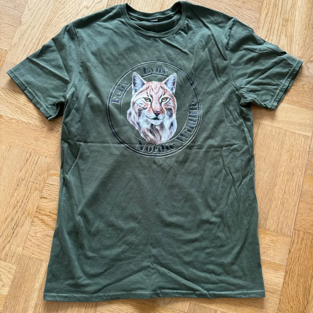 Säljer en grön t-shirt med ett coolt lodjurstryck på framsidan. T-shirten är i bomull och har en normal passform med korta ärmar. Perfekt för vardagsbruk eller en avslappnad dag ute i naturen. 🐾. T-shirts.