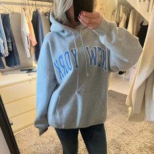 Grå hoodie med New York-tryck - Säljer en supermysig grå hoodie med stort 'New York'-tryck i blått och vitt. Står ingen storlek men skulle säga l-xl, då den är väldigt oversized!!💙🗽