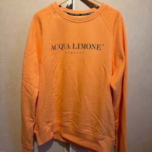Orange sweatshirt från Acqua Limone - Säljer en snygg orange sweatshirt från Acqua Limone i storlek XL. Tröjan har ett klassiskt tryck med märkesnamnet på framsidan och en cool citronlogga på baksidan. Perfekt för en avslappnad stil och passar bra till både jeans och joggers. Skön och bekväm för vardagsbruk! 