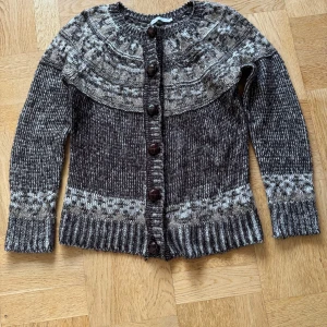 Grå stickad kofta från ONLY - Säljer en superfin brun stickad kofta från ONLY med ett snyggt mönster i brunt och vitt. Koftan har långa ärmar och knappar framtill, perfekt för kyliga dagar. Den är både mysig och stilren, perfekt för höst och vinter! 🍂❄️