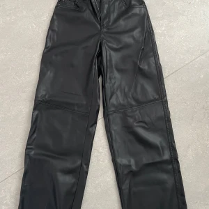 Svarta byxor från Bershka - Snygga svarta byxor från Bershka i storlek XS. De är gjorda av polyuretan vilket ger dem en cool skinnlook. Byxorna har en loose passform och hög midja, perfekt för en trendig stil. Passar både till vardags och fest! Köpta secondhand men aldrig använda av mig! Fint skick