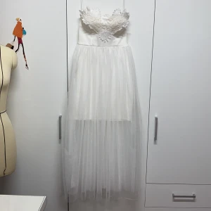 Vit axelbandslös klänning med spetsdetaljer - Säljer en superfin vit axelbandslös klänning med vackra spetsdetaljer på bysten. Kjolen är i ett lätt och luftigt material som ger en drömmig känsla. Perfekt för sommarens fester eller kanske till studenten. Klänningen har en dragkedja i ryggen för enkel påklädning. 🕊️ Använt bara en gång. Storleken är S men sitter mer som XS