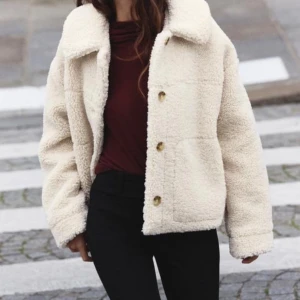Beige teddyjacka med knappar - Supermysig beige teddyjacka med stora knappar framtill. Perfekt för höst och vinter när du vill hålla dig varm och stilren. Jackan har en avslappnad passform och långa ärmar, vilket gör den idealisk för lager-på-lager. Ett måste i garderoben för kyliga dagar!