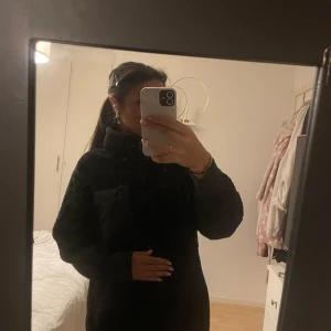 Svart teddyjacka med dragkedja - Mysig svart teddyjacka i fleece med dragkedja framtill. Perfekt för kyliga dagar med sin varma och gosiga känsla. Jackan har en praktisk bröstficka med dragkedja för säker förvaring av småsaker. En stilren och bekväm jacka för både vardag och utflykter.