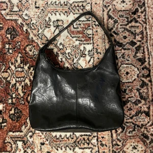 noirvere axelväska i skinn  - Säljer denna stilrena svart axelväska i skinn från noirvere. Väskan har en praktisk storlek och kommer med en matchande liten necessär inuti. Perfekt för vardag och rymmer det mesta du behöver. Den har en magnetknapp för enkel stängning. Köpt för 500kr, aldrig använd.