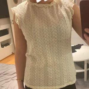Créme Vit topp från Holly & Whyte - Säljer en söt vit topp från Holly & Whyte by Lindex i storlek XS. Toppen har ett vågigt mönster och volangdetaljer vid ärmarna. Perfekt för vår och sommar! 🕊️