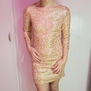 Glittrig kortklänning i guld - Superfin, glittrig kortklänning i guld med trekvartsärm. Perfekt för fest eller nyår! Klänningen har ett snyggt leopardmönster med paljetter som verkligen fångar ljuset. Den är i mycket bra skick och passar perfekt för en glamorös kväll.