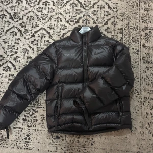 Nike Nocta jacka  - Säljer en snygg svart dunjacka från Nike Nocta i mycket bra skick. Jackan har en stor Nike-logga på ryggen och en mindre på bröstet. Den är perfekt för kalla dagar med sin pufferdesign och dragkedja framtill. Passar både till vardags och sportiga aktiviteter. Passar i S/M ovh är lite använd. Kontakta mig vid mer info.