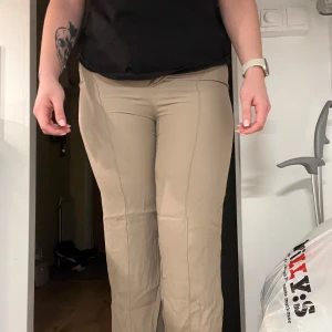 Beige byxor från Zara - Säljer ett par snygga beige byxor från Zara. De är högmidjade och har en slim passform som ger en stilren look. Perfekta för både vardag och fest! Byxorna är i mycket bra skick och har en dragkedja framtill. Storlek är M. 