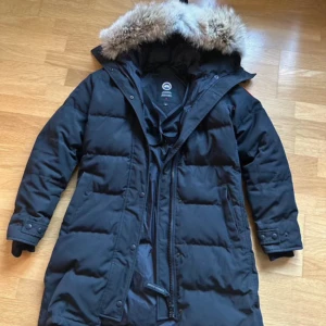Svart dunjacka från Canada Goose - Säljer en svart äkta dunjacka från Canada Goose i mycket bra skick. Jackan har en stor huva med pälsdetaljer och långa ärmar. Perfekt för kalla vinterdagar med sin varma och skyddande design. Dragkedja framtill och märkeslogga på ärmen. Har lagt den för absolut lägsta priset nu, först till kvarn!!!