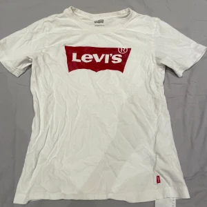 Vit t-shirt från Levi's - Säljer en klassisk vit t-shirt från Levi's med det ikoniska röda logotyptrycket på bröstet. Perfekt för en avslappnad stil och passar till det mesta. Korta ärmar.