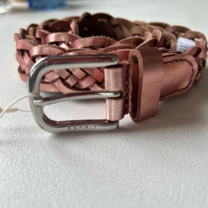 Esprit rosa bälte 105cm med prislappen  - Snyggt flätad läderbälte från Esprit. Bältet har en silverfärgad spänne med Esprit-logotypen. Bältet är oanvänt och kommer med originalprislapp. mått 1050*25 mm  buffalo läder  ordinarie pris 259 kr