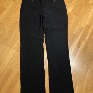 Kostymbyxor  - Svarta byxor med knappar och hällor en bit ner på linningen  Raka ben 