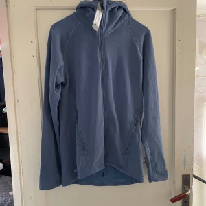 Blå träningsjacka från Funktion - Säljer en blå träningsjacka från Funktion i storlek S. Perfekt för löpning och inomhussporter. Jackan har dragkedja och huva, vilket gör den både praktisk och bekväm. Materialet är mjukt och stretchigt, idealiskt för träning. Passar bra för vår och höst.