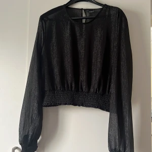 Svart glittrig blus från Gina tricot - Snygg svart blus från   Gina tricot med glittrigt material som ger en festlig touch. Den har långa ärmar och en elastisk midja som ger en fin passform. Perfekt för en utekväll eller festlig tillställning!
