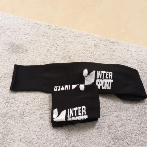Svarta strumpor från Intersport - Säljer ett par svarta strumpor från Intersport. De är i nyskick och har en vit logga på skaftet. Perfekta för träning eller vardagsbruk. Strumporna är bekväma och stretchiga.