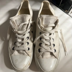 Vita Converse All Star sneakers - Säljer ett par klassiska vita Converse All Star sneakers. De har en tidlös design med snörning och är tillverkade i slitstarkt canvasmaterial. Skorna är i välanvänt skick med lite smuts på sulan, men de har fortfarande mycket liv kvar. Perfekta för både vardag och fest!