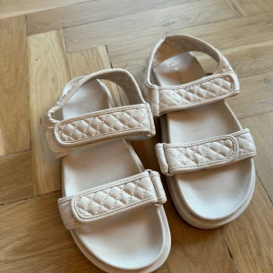 Beige quiltade sandaler - Säljer ett par snygga beige sandaler med quiltad design. De har justerbara remmar med kardborre för perfekt passform. Perfekta för sommaren och tidig höst. aldrig använda. 