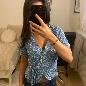 Söt blå topp med blommor - Söt blommig figursatt topp man kan knyta för att justera hur tight man vill den ska sitta på midjan, från Lindex, använd endast 1 gång 🩵