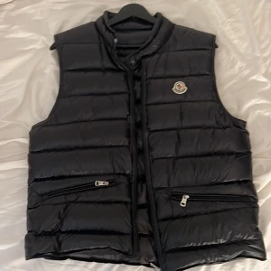 Svart dunväst från Moncler - Moncler gui Säljer en snygg och stilren svart dunväst från Moncler. Västen har en quiltad design med dragkedja framtill och två praktiska fickor med dragkedjor. Perfekt för kyliga dagar när du vill hålla stilen. Pris går att diskutera 