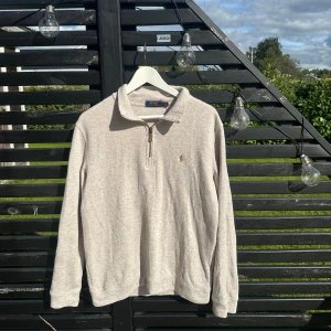 Beige tröja från Ralph Lauren - Säljer en snygg beige tröja från Ralph Lauren. Den har en dragkedja vid halsen och det klassiska Ralph Lauren-märket broderat på bröstet. Perfekt för en stilren och avslappnad look. Passar bra till både vardag och lite finare tillfällen.