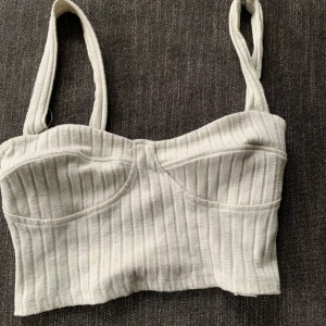 Grå ribbad korsettopp - Säljer en snygg grå ribbad korsettopp med breda axelband. Toppen har en tight passform och är perfekt för både vardag och fest. Den är i ett mjukt och bekvämt material.