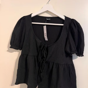 Topp med knytdetalj - Svart kortärmad topp med knytdetalj framtill från ginatricot  Kan användas som en topp eller en liten cardigan Aldrig använd med prislapp kvar  Nypris 279kr