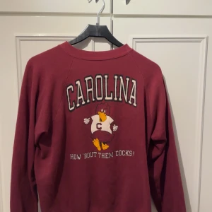 Vinröd Carolina sweatshirt - Säljer en vinröd collegetröja från usa med texten ’CAROLINA’. Tröjan har långa ärmar och är perfekt för en avslappnad stil.