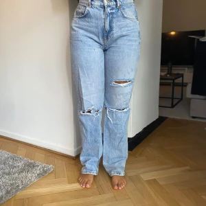 Ljusa jeans med slitningar från gperfect jeans - Säljer ett par ljusa jeans från Gina tricot i storlek 36. De är högmidjade och har en straight passform. Jeansen har coola slitningar på framsidan som ger en avslappnad och trendig look. Perfekta för både vardag och fest!