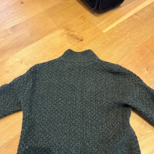 Grön stickad tröja från Chevalier - Säljer en snygg mörk grön stickad tröja från Chevalier. Tröjan har ett diskret mönster och en liten logotypdetalj på ärmen. Perfekt för kyliga dagar med sin varma och bekväma design. Passar bra till både jeans och chinos.