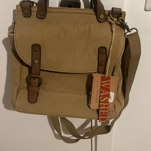 Beige axelväska med bruna detaljer” Feel ” - Snygg beige axelväska med bruna läderdetaljer och justerbar axelrem. Väskan har en praktisk design med flera fack och stängs med ett lock och spännen. Perfekt för vardagsbruk och ger en stilren look.