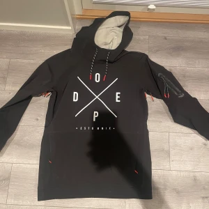 Dope jacka  - Säljer en svart skidjacka från Dope med vit text och grafiskt tryck på framsidan. Jackan har en huva med snörning och en praktisk ficka på ärmen till mobil eller liftkort mm. Perfekt för en skidtur. Använd en restur i 4 dagar så väldigt bra skick. Passar M/L