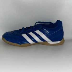 Blå Adidas inomhusskor  - Snygga blå fotbollsskor från Adidas med vita ränder och en gummisula. Skorna har snörning och är perfekta för futsal, handboll, innebandy mm.