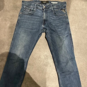 Replay anbass  - Snygga blå jeans från Replay, modell Anbass. De har en klassisk femficksdesign med dragkedja och knapp. Jeansen har en modern passform och är perfekta för en stilren look. Blivit slitet där vid gylfen. 30/32 size 