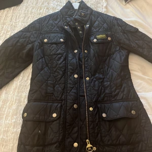 Svart quiltad jacka från Barbour - Säljer en snygg svart quiltad jacka från Barbour med dragkedja och knappar. Jackan har flera praktiska fickor och en klassisk design. Perfekt för kyligare dagar! Finns ett jätte litet hål i högra fickan och bälte saknas. Men utöver det så är den jätte fin. PRIS KAN DISKUTERAS 