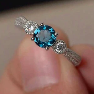 Ring med blå sten och vita kristaller - Ny och oanvänd!  Elegant ring med en stor blå sten i mitten, omgiven av två mindre vita kristaller. Ringen har en glittrig design med små vita stenar längs bandet, vilket ger en lyxig känsla. Kommer i en fin liten tygpåse