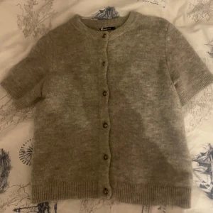 Grå kofta från Gina Tricot - Säljer en stilren grå kofta från Gina tricot. Koftan har korta ärmar och knappar framtill. Perfekt för lager-på-lager under kyligare dagar. 🧥