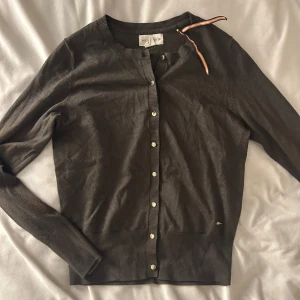 Brun/grön  kofta från Holly & Whyte - Säljer en stilren brun kofta från Holly & Whyte med knappar framtill. Koftan har långa ärmar och en ribbad kant vid ärmslut och nederkant. Perfekt för en elegant och avslappnad look. Knappt använd så i bra kvalitet!