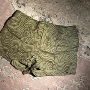 Gröna shorts i y2k stil  - Snygga gröna shorts från H&M med ett unikt vågigt mönster. De har en bekväm passform och är perfekta för varma dagar. Shortsen har praktiska fickor och en knappdetalj i midjan.