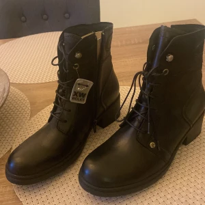 Svarta boots från Wolky - Snygga svarta boots från Wolky med snörning och dragkedja. Tillverkade i skinn med en robust sula och klack. Perfekta för en stilren look.