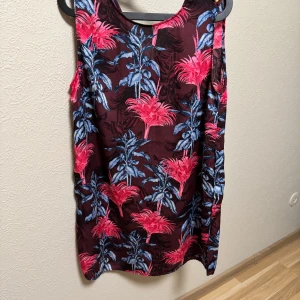Blommig klänning från Holly & Whyte - Snygg ärmlös klänning från Holly & Whyte med ett färgstarkt blommönster i rosa och blått på en vinröd bakgrund. Perfekt för att sticka ut med stil! 🌺
