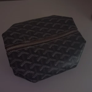 Svart mönstrad necessär - Snygg svart necessär med ett unikt mönster och dragkedja. Perfekt för att hålla ordning på dina småsaker när du är på språng.