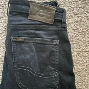 Mörkblåa jeans från Lee - Snygga svarta jeans från Lee med klassisk femficksdesign och en diskret logga på bakfickan. Jeansen har en smal passform och är perfekta för en stilren look. De är tillverkade i ett slitstarkt material som ger en bekväm känsla hela dagen. Skriv vid funderingar 