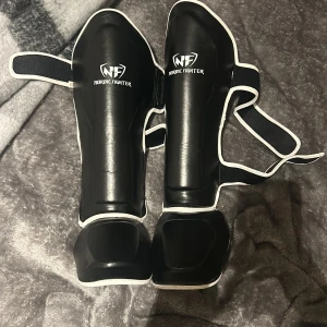 Svarta benskydd från Nordic Fighter - Säljer ett par svarta benskydd från Nordic Fighter.  justerbara remmar för perfekt passform. Perfekta för kampsportsträning. Storlek M, säljer pga att de inte används 