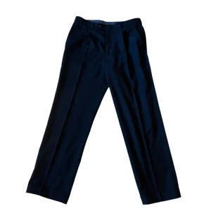 Svarta kostymbyxor - Eleganta svarta kostymbyxor med en klassisk straight passform. Perfekta för en stilren look. Byxorna har en diskret dragkedja och knappar framtill.