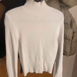 Vit stickad polotröja - Säljer en stilren vit stickad polotröja med ribbade detaljer vid hals och nederkant. Perfekt för kyligare dagar och enkel att matcha med olika outfits. Skön och varm!