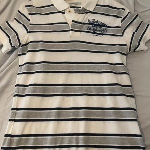 Randig pikétröja från Peak Performance - Säljer en stilren randig pikétröja från Peak Performance i vitt, grått och svart. Tröjan är i perfekt skick 